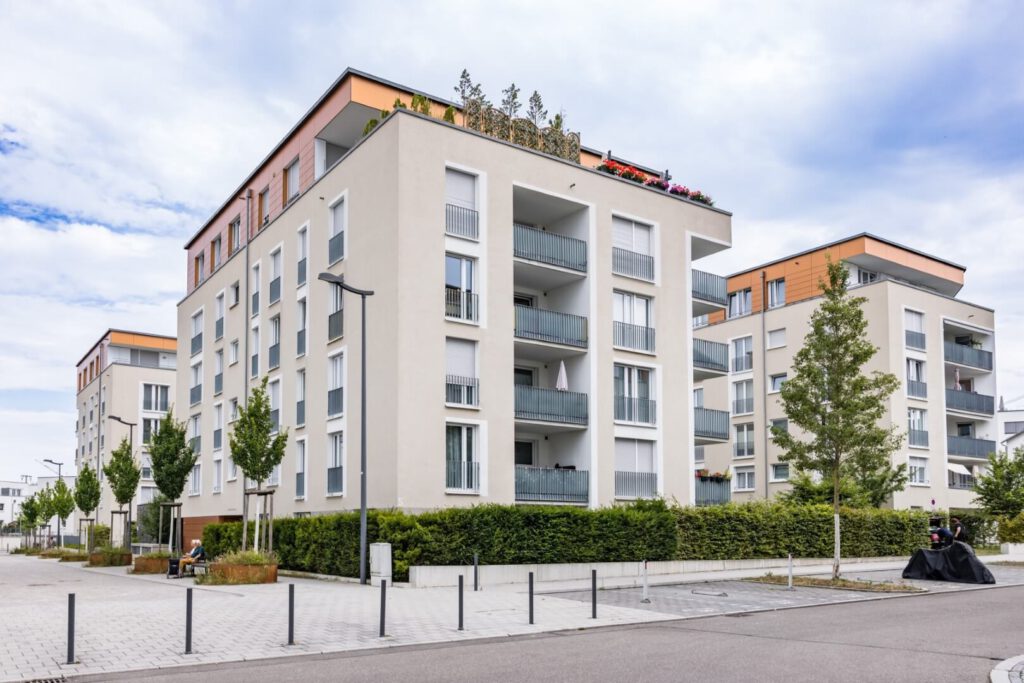 Gepflegtes Mehrfamilienhaus an einer Straße mit Parkbereich und Vorgarten mit kurzer Hecke