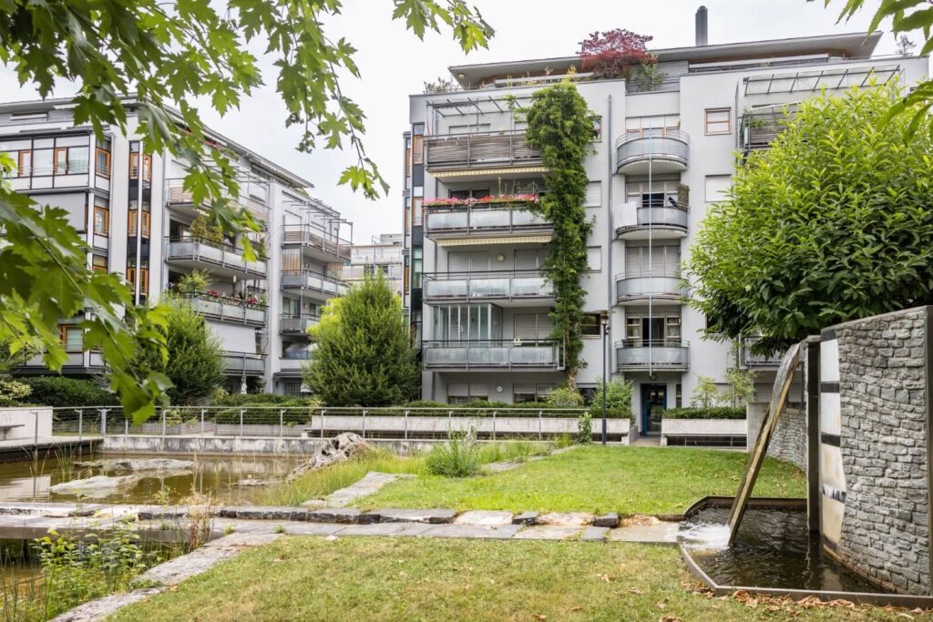 Gepflegtes Mehrfamilienhaus im Hintergrund, Brunnen, Innenhof und Rasenstück im Vordergrund