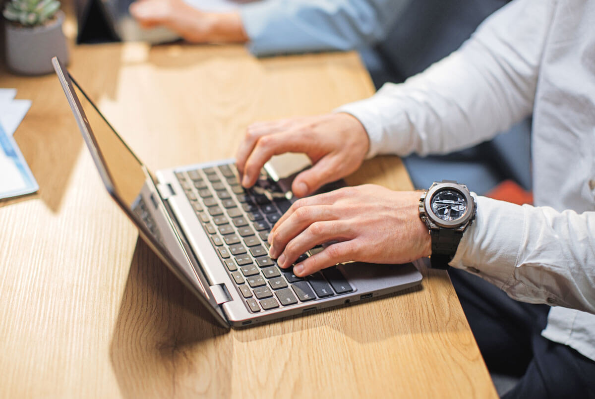 Nahaufnahme von männlichen Händen, die auf einem Laptop tippen
