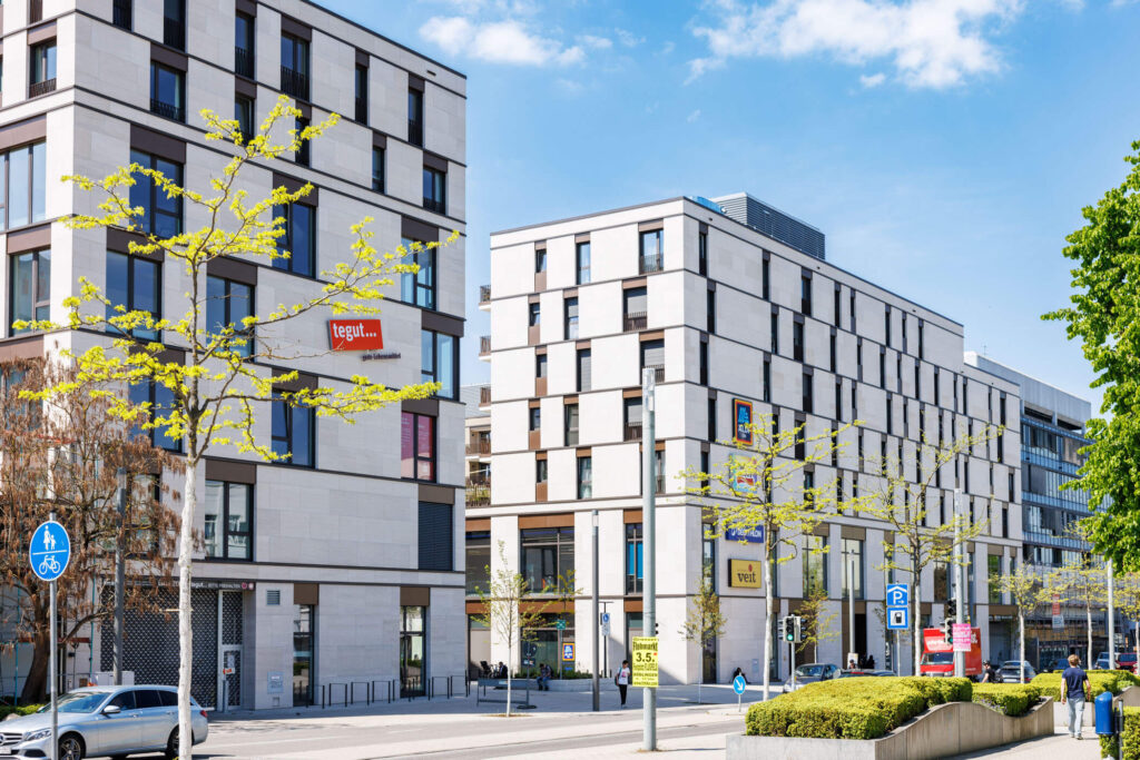 Ein modernes Wohn- und Gewerbequartier mit Menschen, Rabatte und einer angrenzenden Straßenseite
