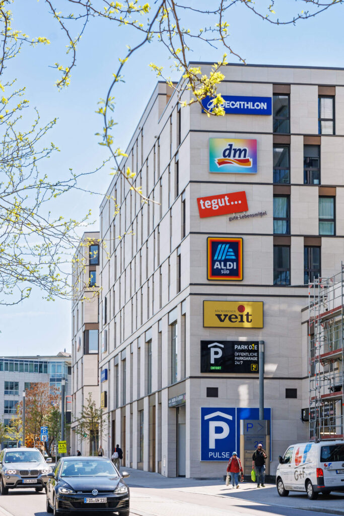 Ein modernes Wohn- und Gewerbequartiers mit prominenten Schildern aller Geschäfte am Gebäude umgeben von Straße