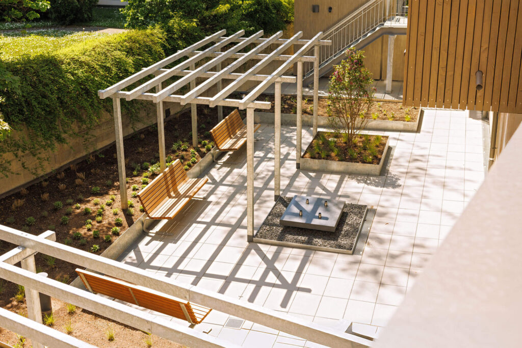 Schattiger, begrünter Innenhof mit Bänken unter einer Pergola aus einem Gebäude herab fotografiert